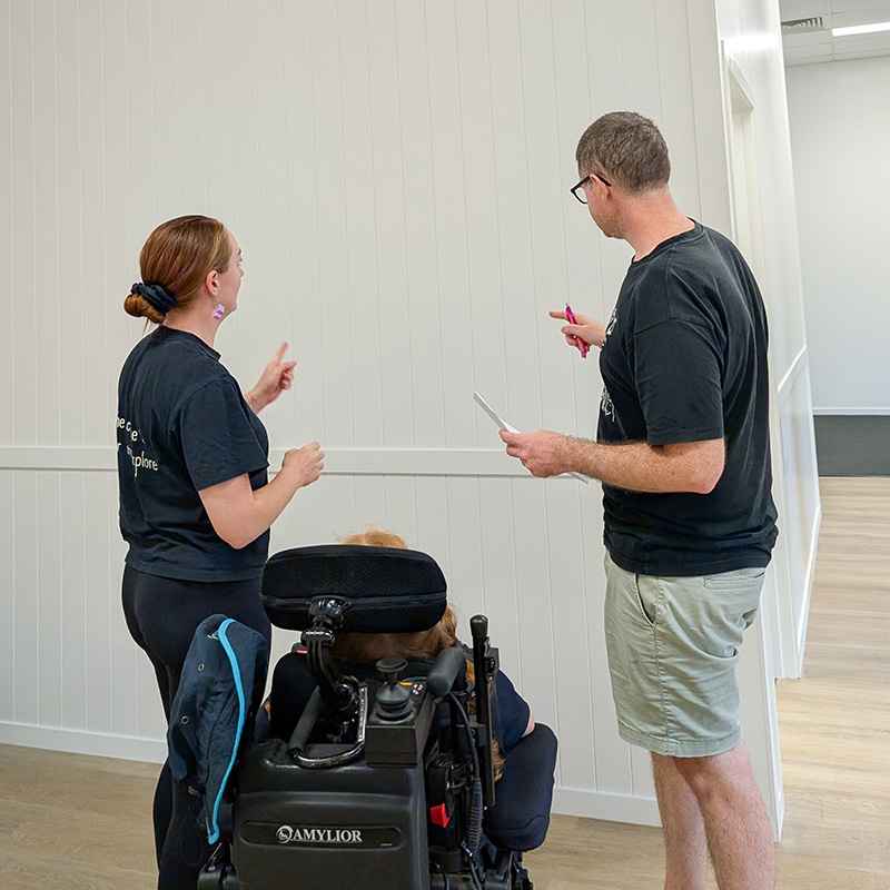 A man and woman, and child in a wheelchair are discussing options for a blank wall.